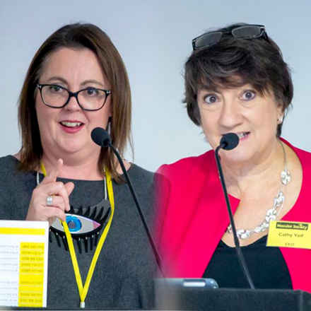 Cathy Yelf and researcher at conference speaking into microphones